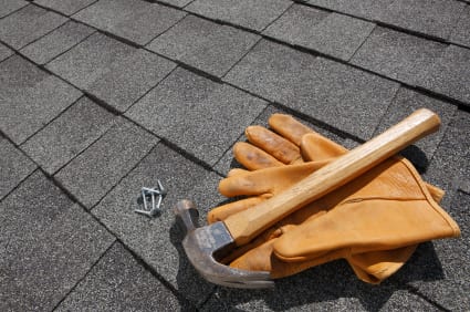 A hammer and leather gloves next to nails on a shingled roof, indicating ongoing roof improvement or repair work by BG Roofing Springfield MO.