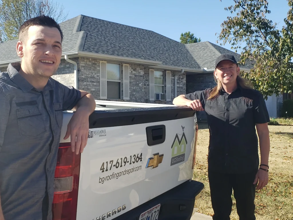 Two people standing beside a bg roofing company pickup truck in front of a house after servicing roof maintenance work.